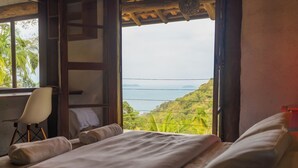 A bedroom with a bed, a chair, and a view of a lush landscape through a window. - Felix Ocean View, Ubatuba, Sao Paulo, Brazil. (Ubatuba)