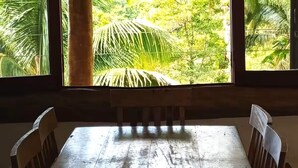 A wooden dining table with chairs, large windows with a view of a tropical forest. - Felix Ocean View, Ubatuba, Sao Paulo, Brazil. (Ubatuba)