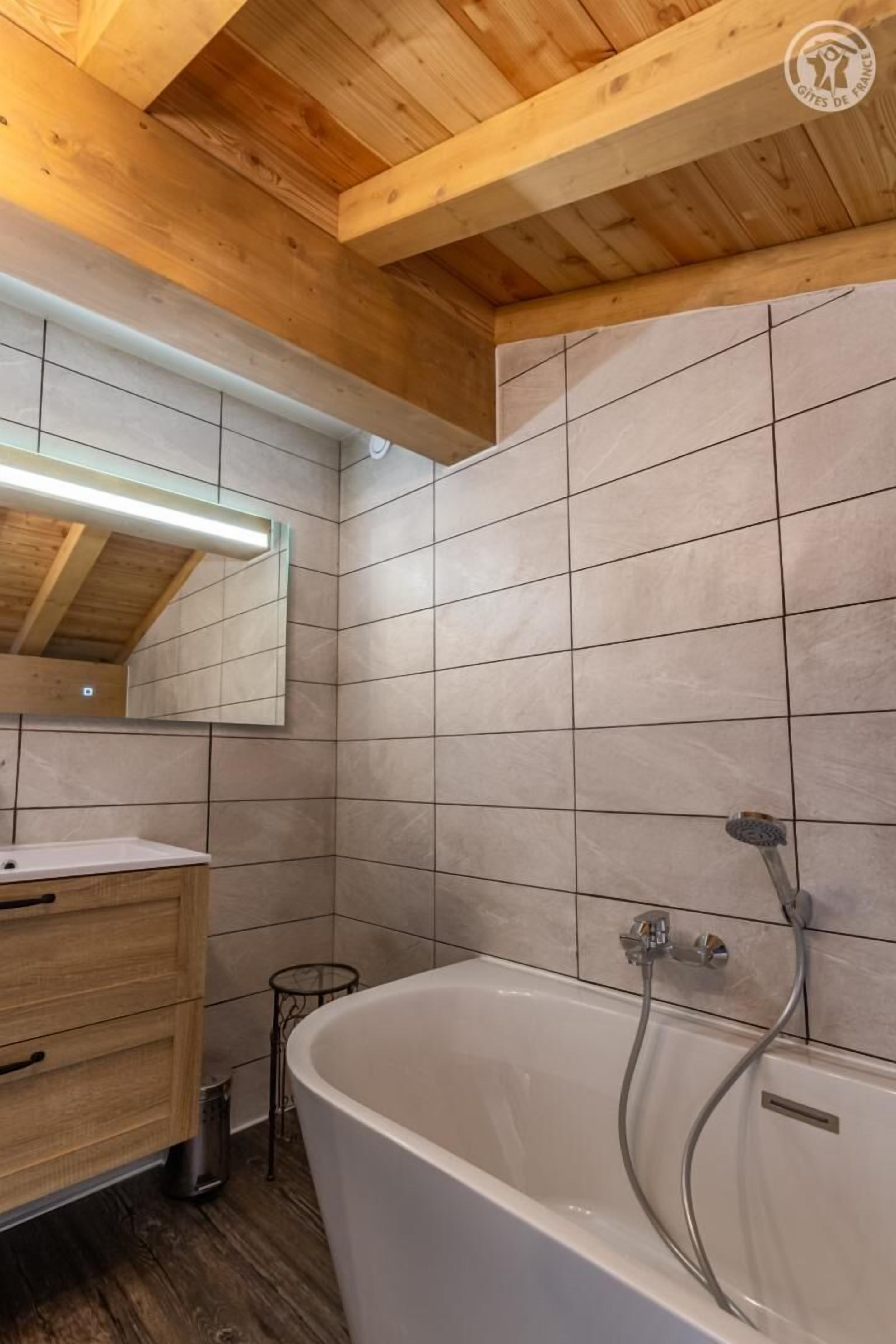 Une salle de bain moderne avec un plafond en bois, une baignoire sur pieds, un meuble-lavabo avec un miroir et des murs carrelés.