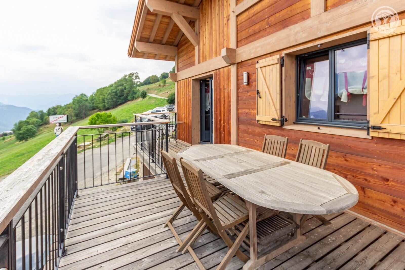 Een houten terras met een tafel en stoelen, met uitzicht op een schilderachtig landschap met bergen en een weg.