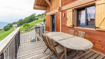 A wooden deck with a table and chairs, overlooking a scenic landscape with a view of the mountains and a road.