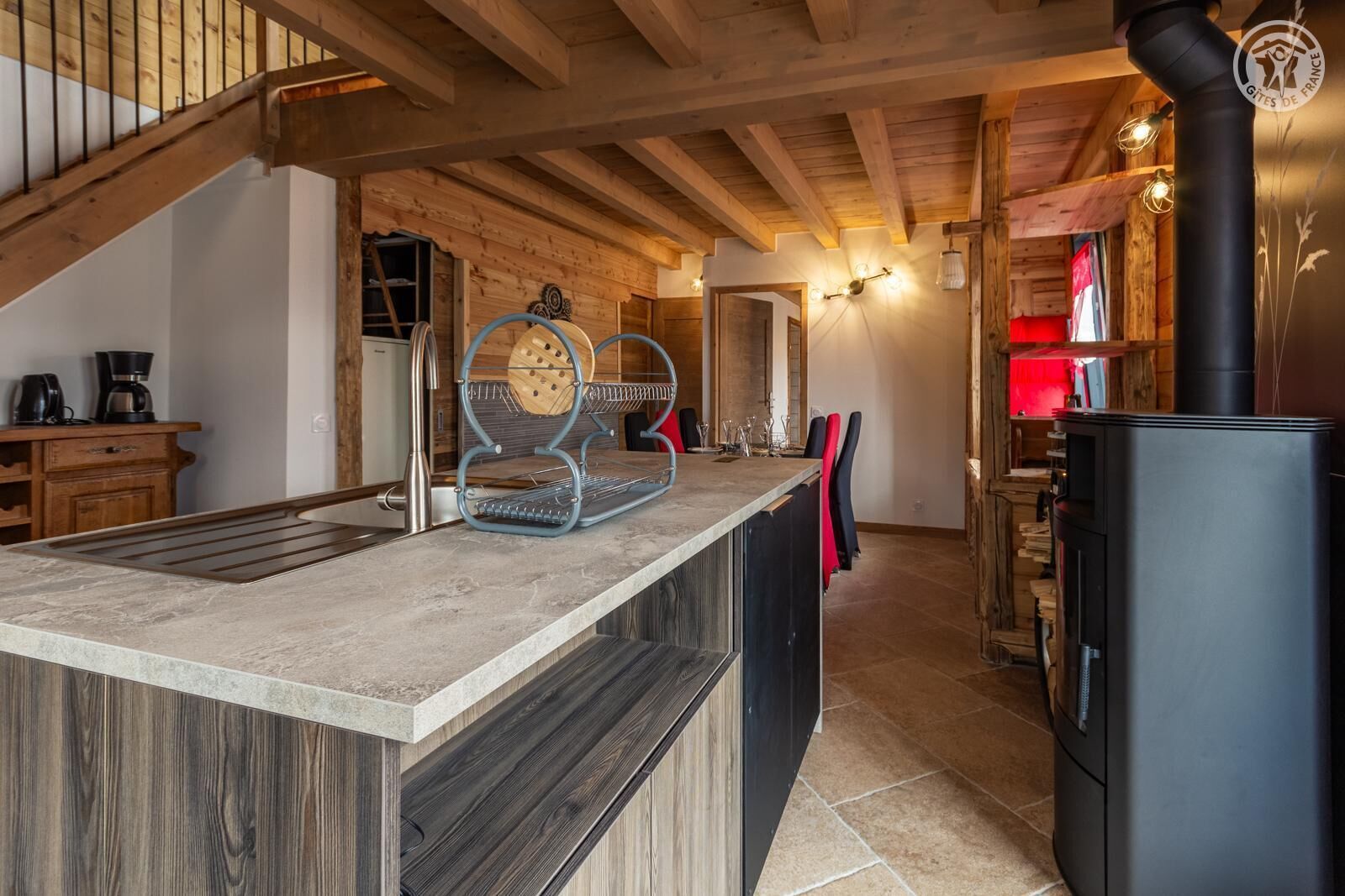 A modern kitchen with a central island, wooden beams, and a black stove.