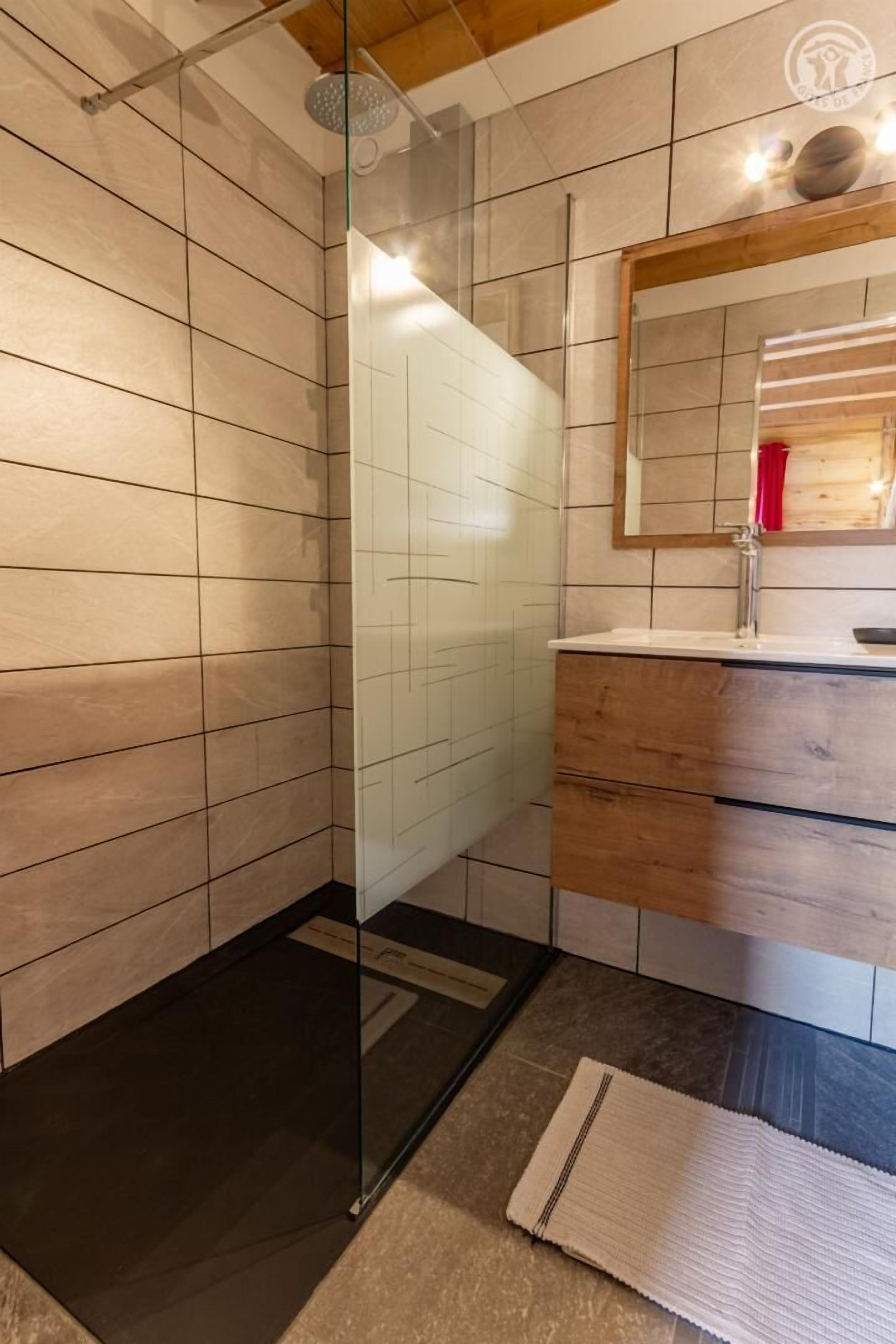 Une salle de bain moderne avec une douche à parois de verre, un meuble-lavabo en bois avec un miroir et un sol carrelé.