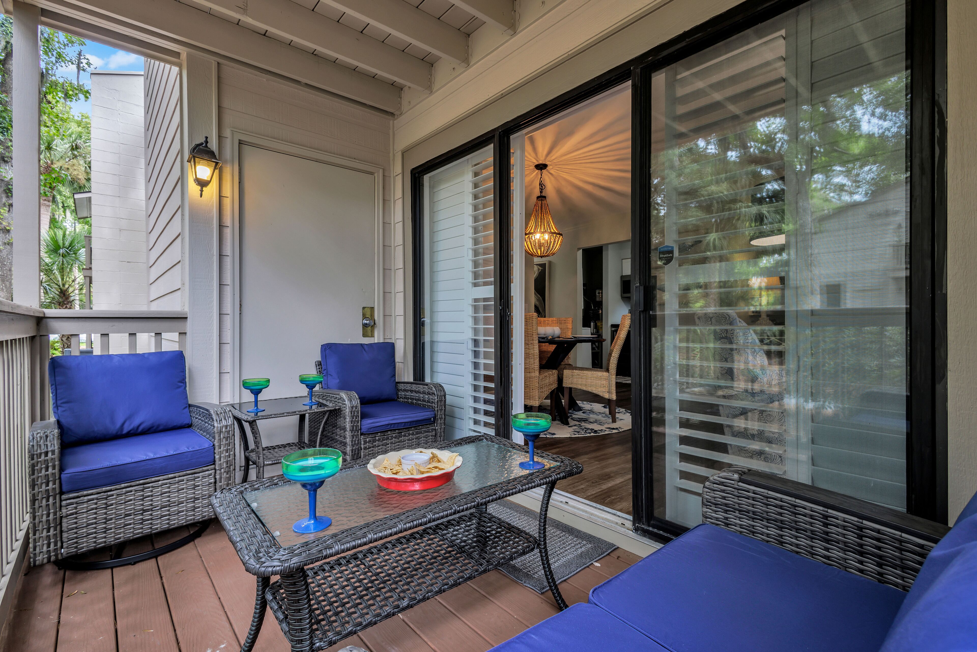 A covered patio area with wicker furniture, blue cushions, and a glass table.
