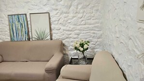 A living room with a stone wall, two framed artworks, a beige sofa, and a small table with a vase of flowers. - Naturastur vacation home (Llanes)