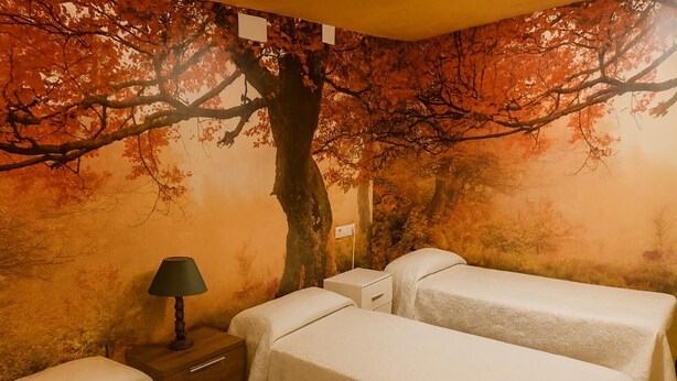 A room with two beds, a nightstand, a lamp, and a mural of a tree. - Naturastur vacation home (Llanes)