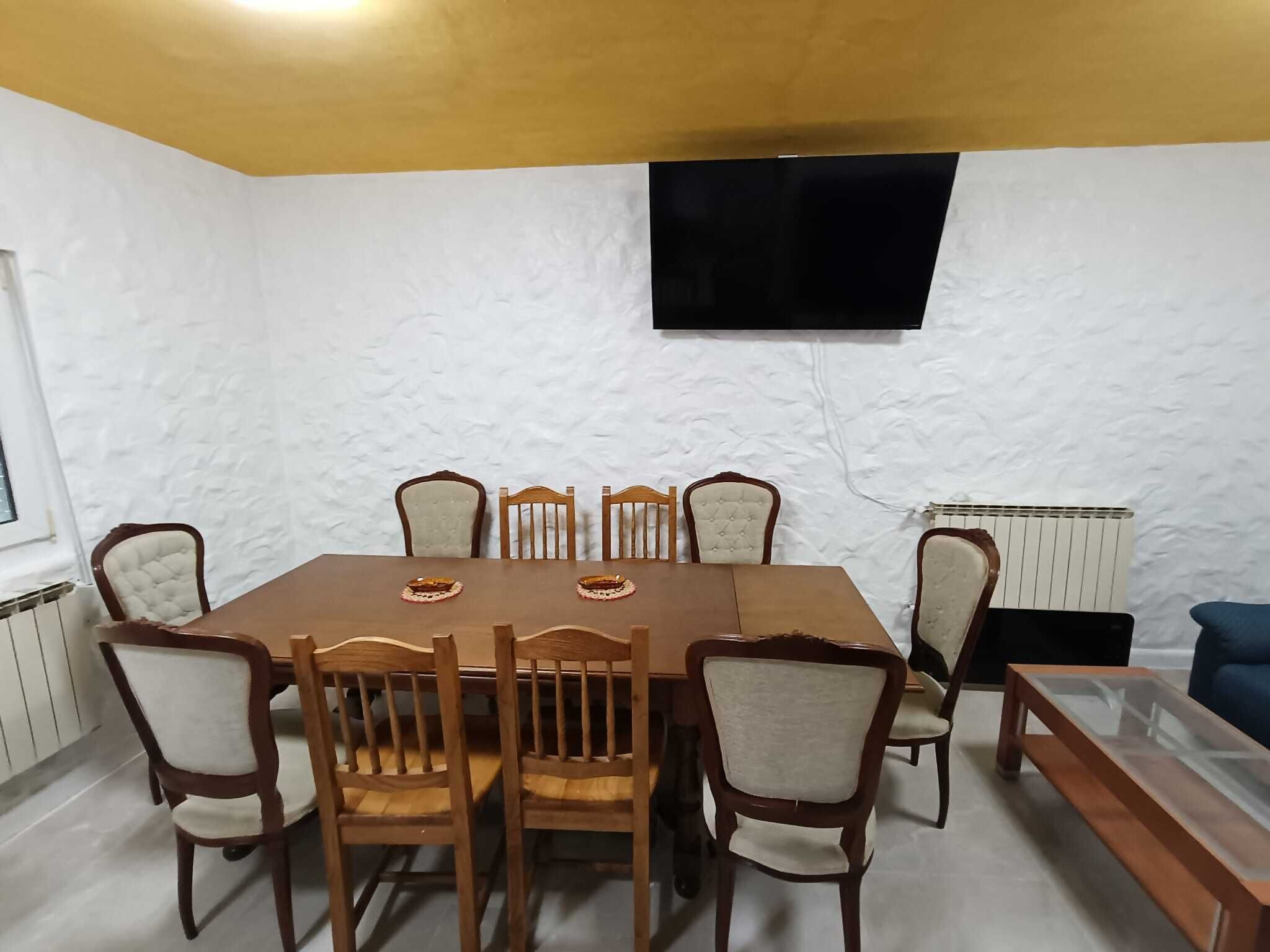 A dining area with a wooden table and chairs, a television mounted on the wall, and a radiator.