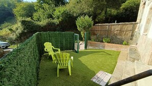 A small backyard with artificial grass, two green chairs, a small tree, and a stone wall. - Naturastur vacation home (Llanes)