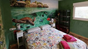 A bedroom with a mural of a sea turtle, a bed with floral bedding, and a window with a view. - Naturastur vacation home (Llanes)
