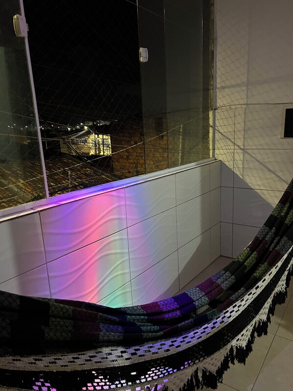 A balcony with a view of a cityscape at night, featuring a hammock and a tiled floor.