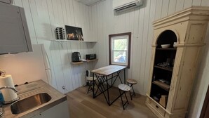 Eine kleine Küche mit Holztisch, zwei Hocker, einer eingebauten Ablage für Küchengeräte und einem weißen Schrank.