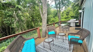 Eine Terrasse mit Korbmöbeln, einem gemusterten Teppich und Grillplatz.