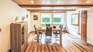 Ein Essbereich mit Holztisch und -stühlen, einem Holzschrank und einem Fenster mit Blick ins Grüne.