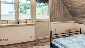 Ein Schlafzimmer mit einem Bett, einem Fenster mit Blick auf Grünflächen und einer schrägen Holzbalkendecke.