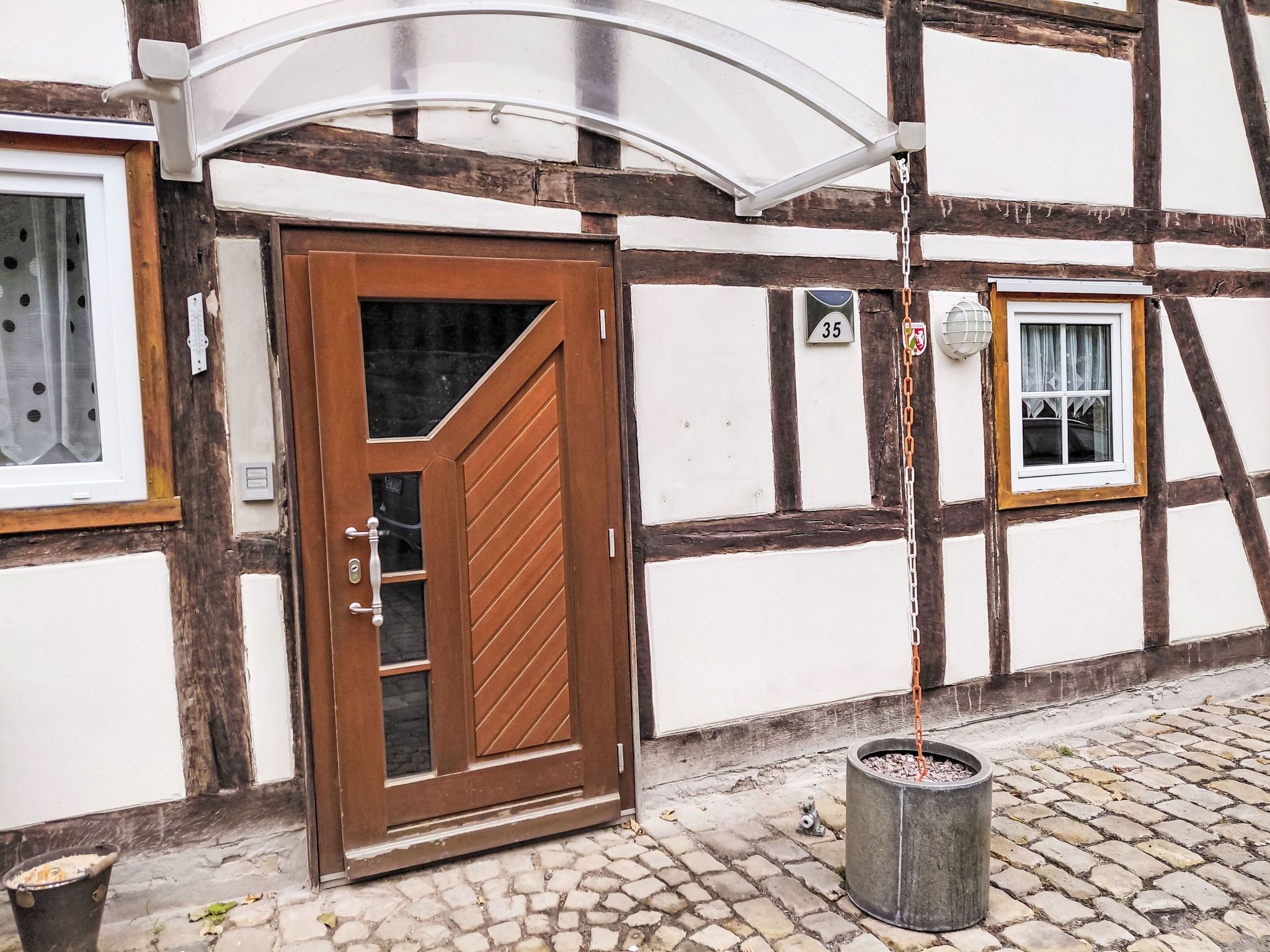 A traditional half-timbered building with a wooden door, a small window, and a potted plant on the cobblestone ground.