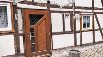 A traditional half-timbered building with a wooden door, a small window, and a potted plant on the cobblestone ground.