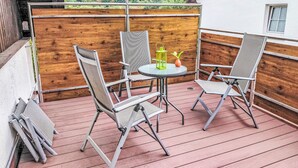 Eine Holzterrasse mit zwei Stühlen und einem Tisch mit Blick auf ein bewaldetes Gebiet.