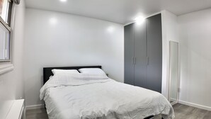 A bedroom with a bed, a wardrobe, and a window. - Sunny House in Queens · Entire Home · Private Parking (Queens)