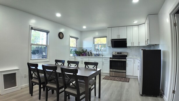 A modern kitchen with white cabinets, a dining table with chairs, and a black refrigerator. - Sunny House in Queens · Entire Home · Private Parking (Queens)