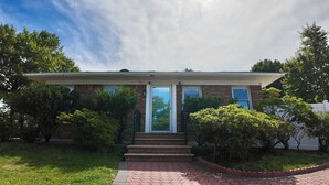 A two-story brick house with a front porch, a garage, and a well-maintained lawn. - Sunny House in Queens · Entire Home · Private Parking (Queens)