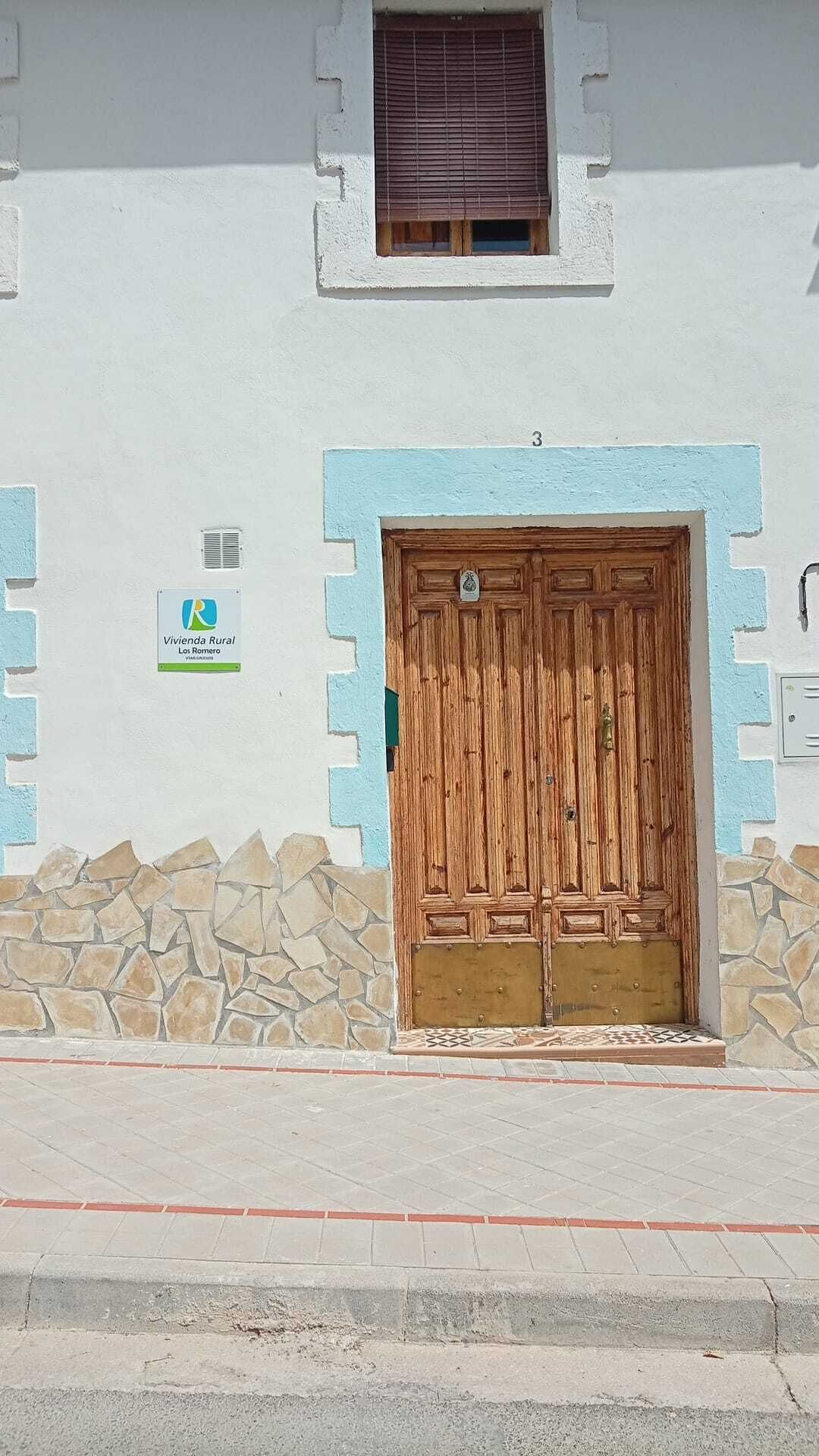A building with a large wooden door, a small window with blinds, and a sign indicating a rural living area.