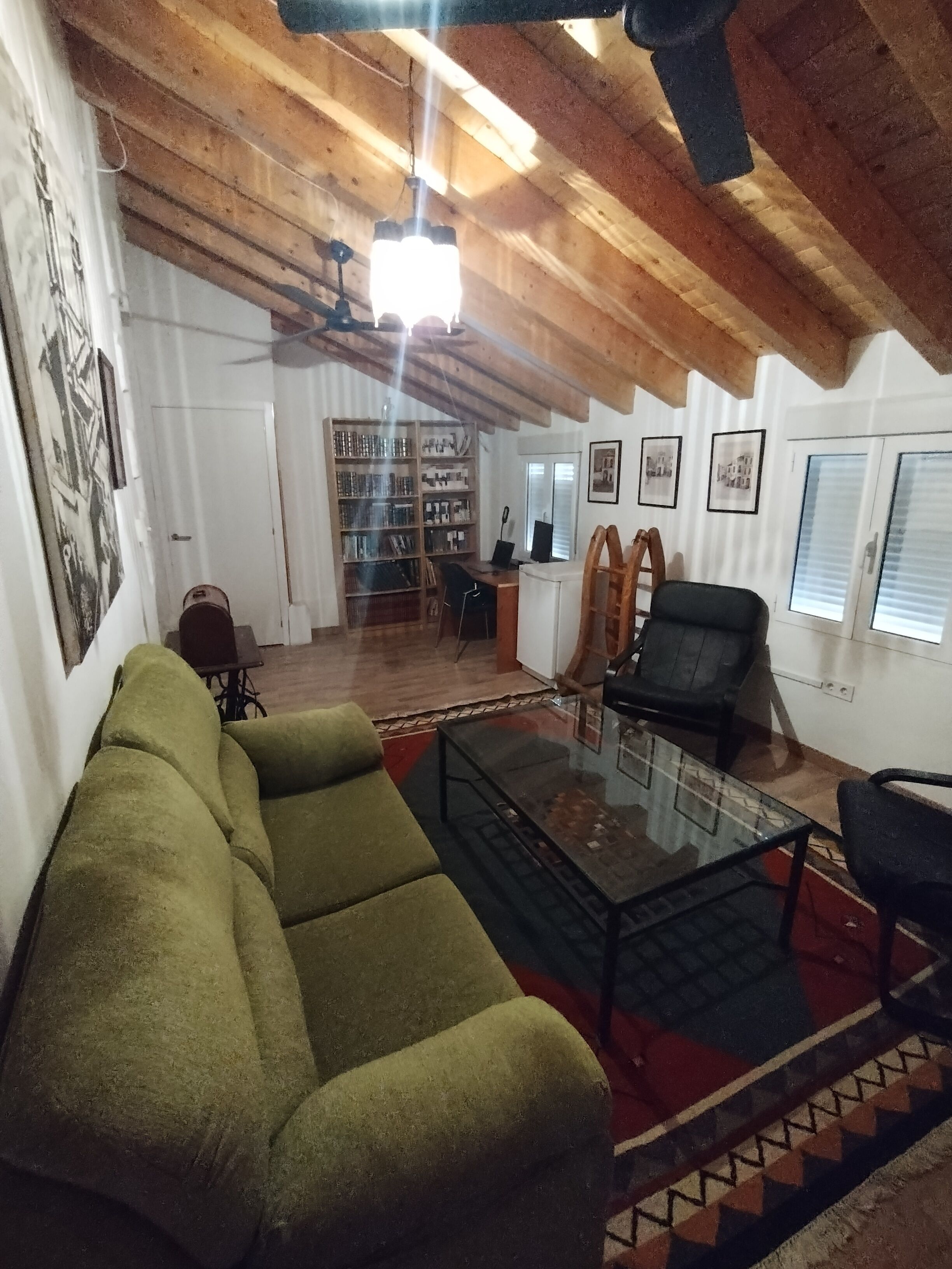 Een gezellige woonkamer met een groene bank, een glazen salontafel en een houten plafond.