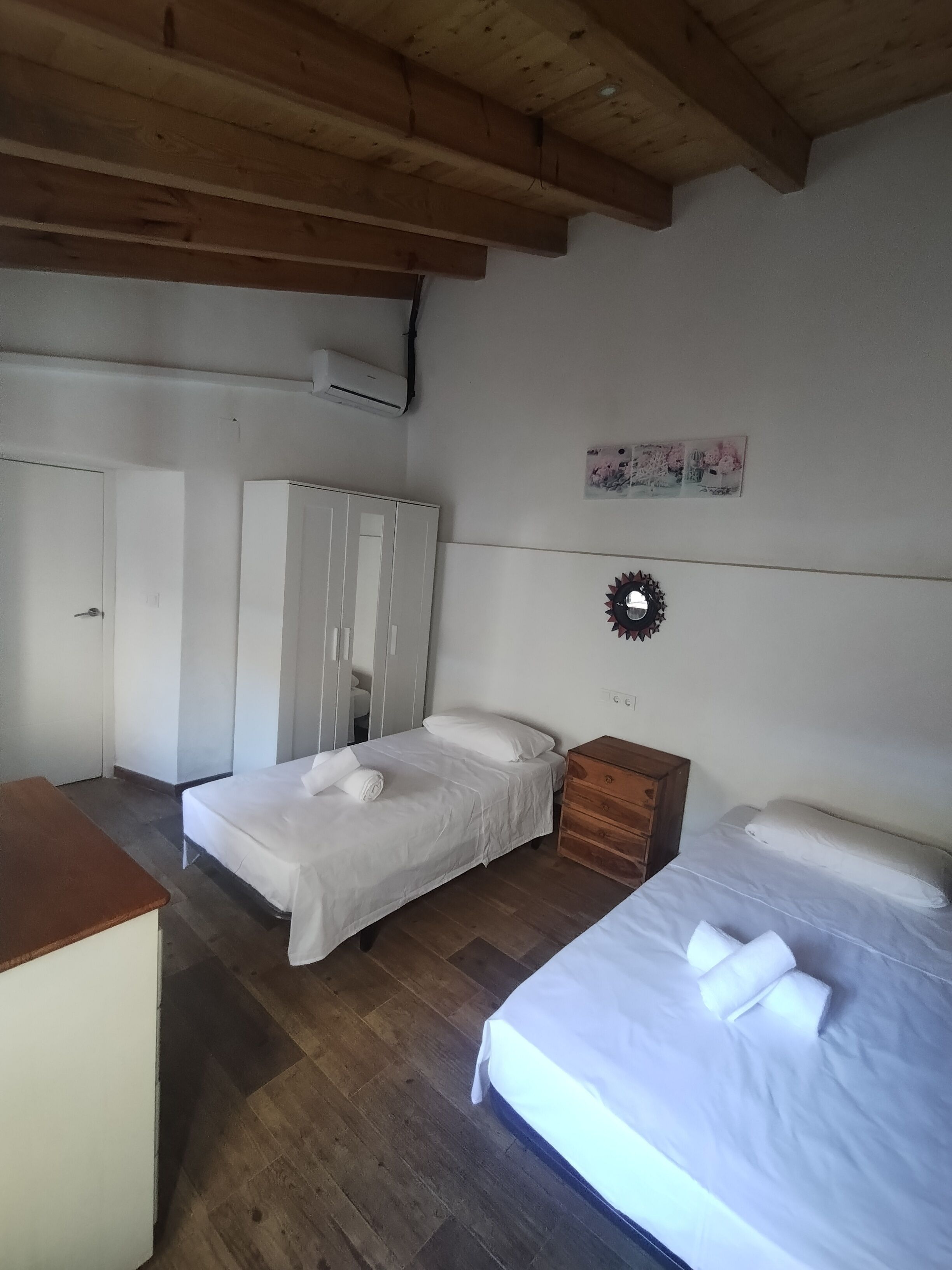 A bedroom with two beds, a wardrobe, a wooden bench, and a wall-mounted air conditioner.