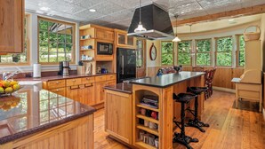 A spacious kitchen with wooden cabinets, a central island, and large windows offering a view of greenery.