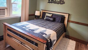 A bedroom with a wooden bed, a window with curtains, a bedside lamp, and a wall decoration.