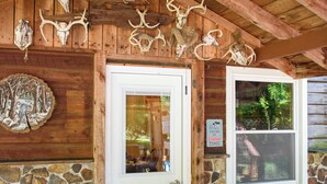 A wooden cabin with a stone wall, a white door, a window, a metal table, and a ceiling fan.
