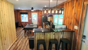 Un interior de madera con una cocina que incluye una barra y taburetes, una mesa de comedor con sillas y un ventilador de techo.