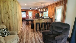 A cozy room with a wooden floor, a sofa, a chair, and a kitchen area with a bar.