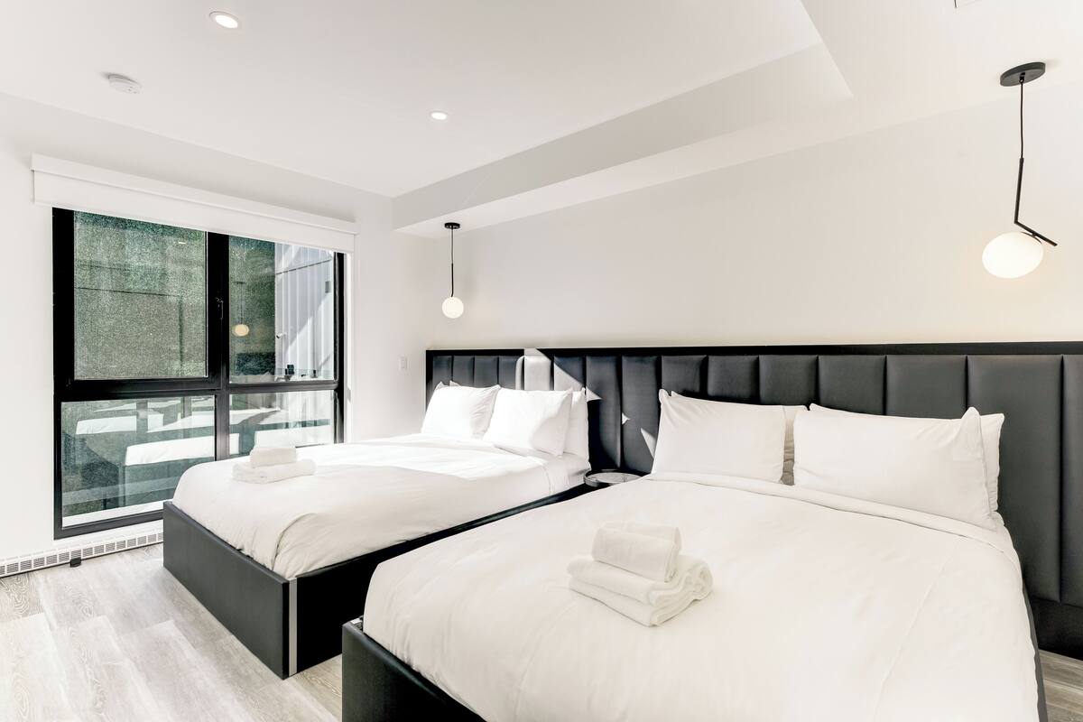 A modern hotel room with two beds, a large window, and a minimalist design.