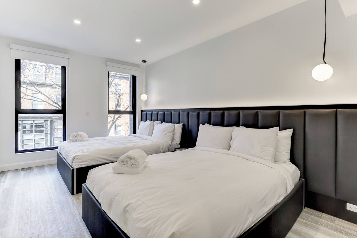 A modern hotel room with two beds, large windows, and a minimalist design.