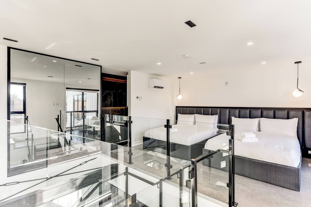 A modern bedroom with a large bed, a glass-enclosed staircase, and a large mirror.