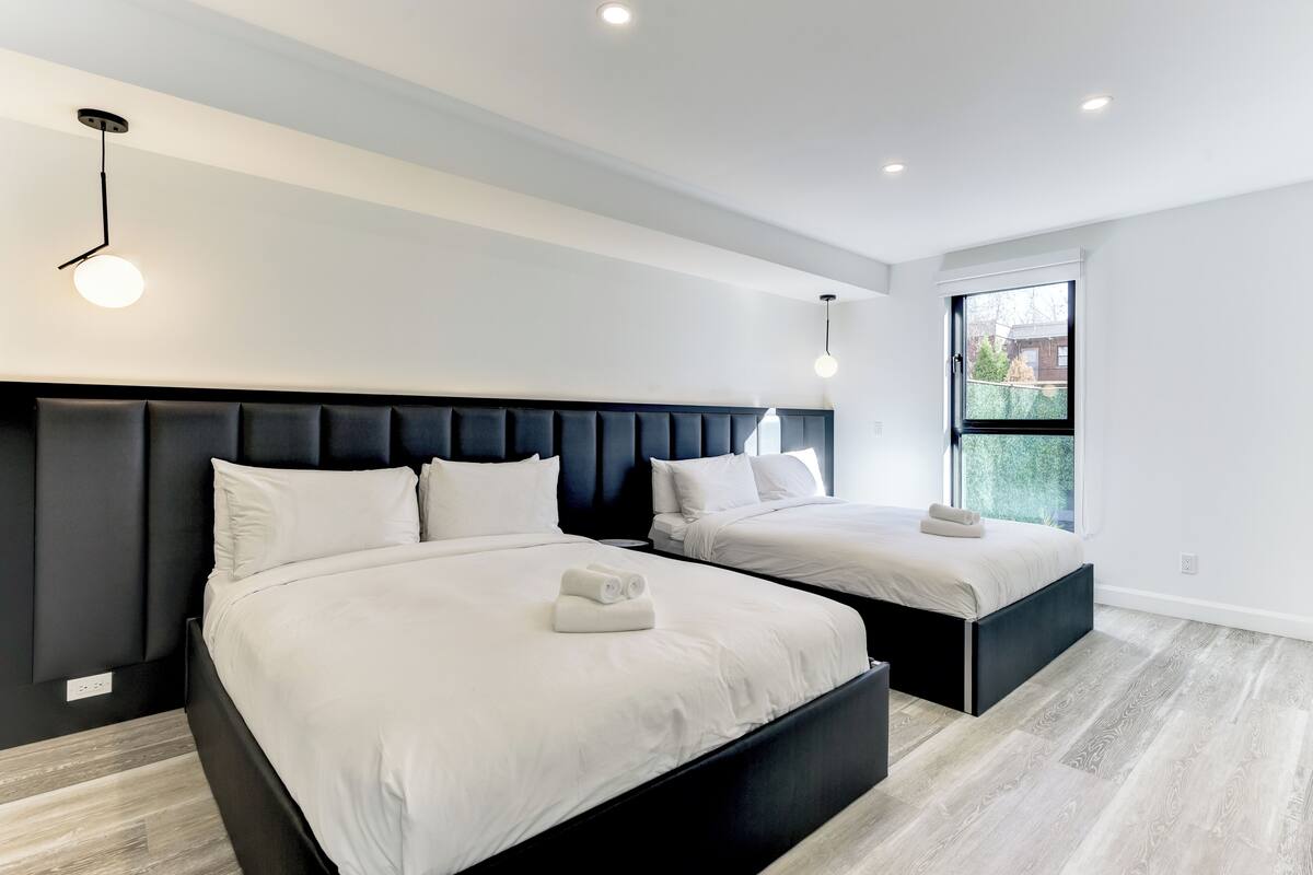 A modern hotel room with two beds, a dark headboard, and a large window.