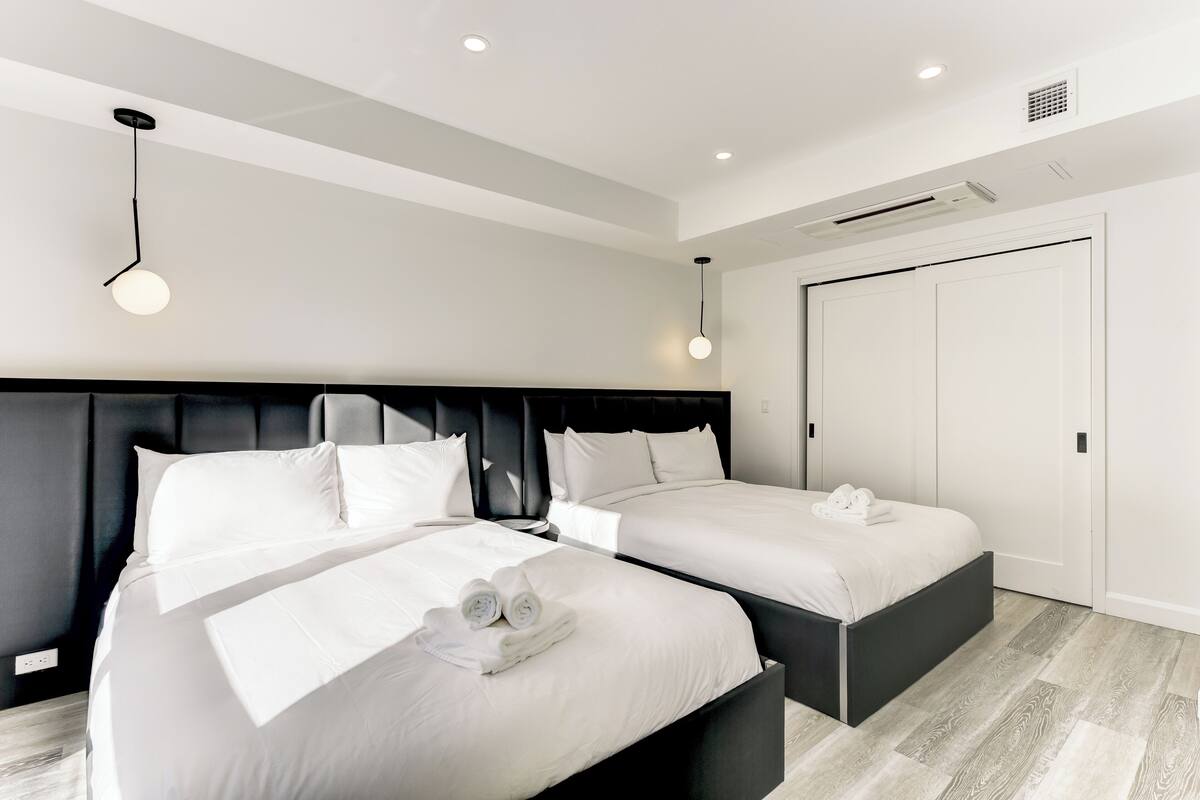 A modern hotel room with two beds, a black headboard, white bedding, and a ceiling light fixture.