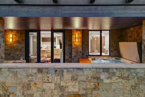 A spa area with a hot tub, stone walls, and a view into a room with a kitchen and bathroom. - Abode at Empire Residences, ski-in/ski-out, hot tub, empire pass (Park City)