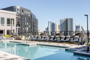 Una piscina en la azotea con sillones de descanso y un horizonte urbano al fondo.