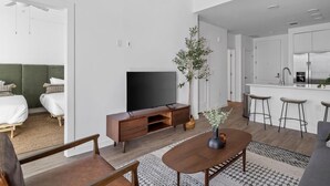 Een moderne hotelkamer met een flatscreen televisie, houten meubels, een eettafel en een keuken met een bar.