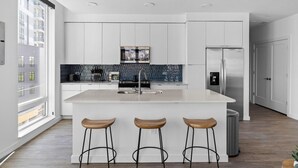 Een moderne keuken met witte kasten, een centraal eiland met krukken, een roestvrijstalen koelkast en een spatwand met blauwe tegels.