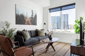 Una sala de estar moderna con un sofá gris, un sillón de cuero marrón, una mesa de centro y un ventanal con vistas a la ciudad.