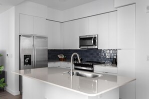 Una cocina moderna con armarios blancos, un refrigerador de acero inoxidable, un microondas y un lavabo con grifo.