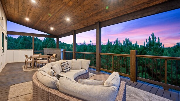 A covered outdoor deck with a curved sofa, a dining table, and chairs. - Hot Tub | Fire Pit | Corn Hole (Broken Bow)