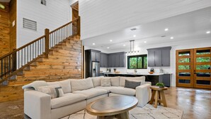 A spacious living area with a large sectional sofa, a round coffee table, and a staircase leading to an upper level. - Hot Tub | Fire Pit | Corn Hole (Broken Bow)