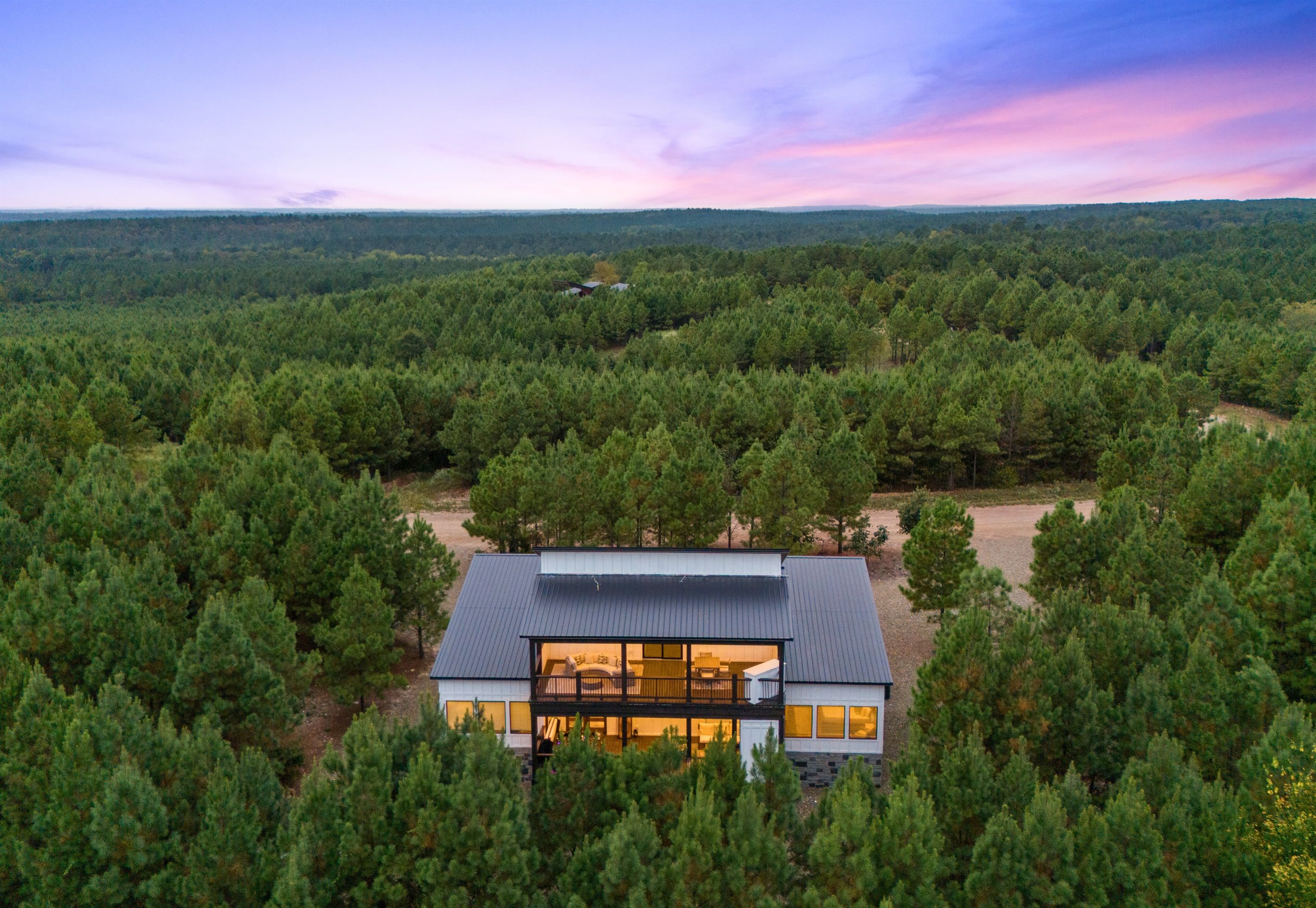 Une maison moderne dotée d’une grande façade en verre, entourée d’une forêt dense.