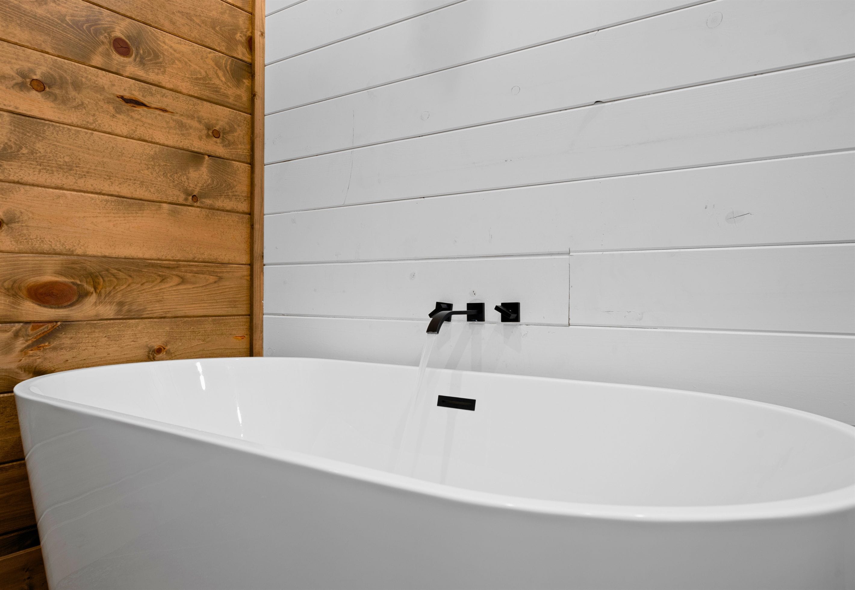 A white bathtub with a black faucet against a wooden wall.