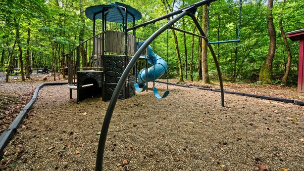 A playground with a slide and swings surrounded by trees. - Creek Bluff Retreat for Large Families and Groups (Broken Bow)