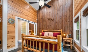 A room with a wooden bed, a ceiling fan, and a wooden wall.
