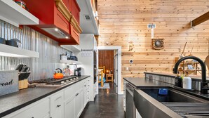 A modern kitchen with white cabinets, a red accent wall, and a wooden ceiling. - Creek Bluff Retreat for Large Families and Groups (Broken Bow)